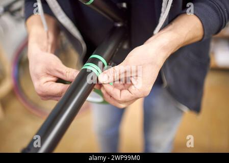 Unerkennbarer Mann, der einen Fahrradrahmen mit Abdeckband für ein individuelles Maldesign in seiner Fahrradwerkstatt vorbereitet, ein handgefertigter kreativer Prozess. Stockfoto