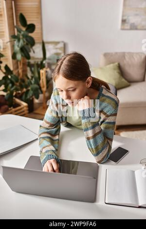 Teenagerin, die sich auf E-Learning konzentriert, mit Laptop und Smartphone auf ihrem Schreibtisch zu Hause, Hausaufgaben Stockfoto
