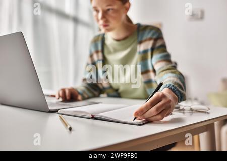 Konzentrierter Teenager, der Hausaufgaben auf dem Laptop in einer häuslichen Umgebung macht, konzentrieren Sie sich darauf, dass Gen z Girl Notizen macht Stockfoto