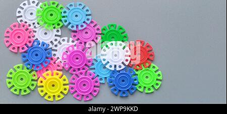 Mehrfarbige Details in Form von Schneeflocken vom Kinderdesigner auf grauem Hintergrund. Rot, gelb, grün, blau, weiß, rosafarbene Kunststoffscheiben Stockfoto