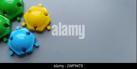 Mehrfarbige Details vom Kinderdesigner auf grauem Hintergrund. Gelbe, grüne, blaue Kunststoffscheiben zur Entwicklung der Feinmotorik von Stockfoto