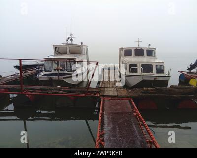 Belgrad, Serbien, 14. Januar 2020 zwei weiße Boote an einem hölzernen Pier fuhren in den Winter. Nebeliges Wetter in Südeuropa. Januar bewölkter Tag Stockfoto