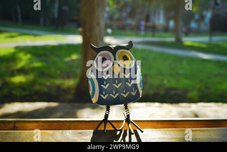 Ein Nahaufnahme-Spielzeug einer überraschten blauen Eule mit bunten Augen steht auf einem Stück Holz im Licht der Abendsonne Stockfoto