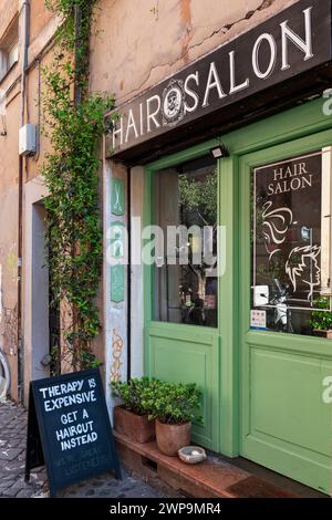 Friseursalon, Eingangstür zum Haidresserladen für Männer und Frauen im Trastevere-Viertel. Ironisches Nachrichtenbanner draußen. Rom, Italien, Europa, EU Stockfoto