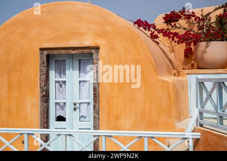 Ein fesselndes traditionelles Santorini-Haus mit einer hellblauen Tür, geschmückt mit lebhaften Bougainvillea-Blumen vor einer Terrakotta-Fassade. Stockfoto