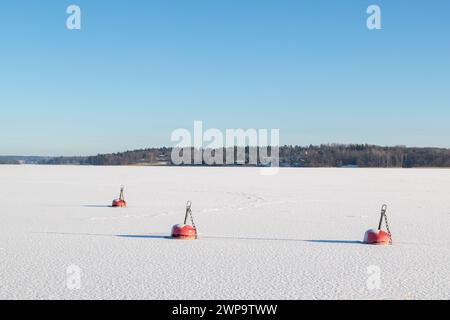 Gefrorener See mit drei roten Bojen am sonnigen Wintertag. Blauer, sauberer Himmel. Stockfoto