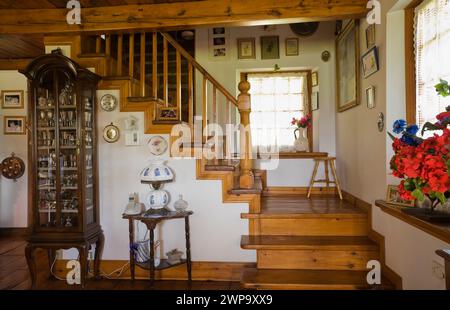 Teilweise Blick auf das Wohnzimmer mit antiken Möbeln und einer Kiefernholztreppe, die zum oberen Stockwerk in einer alten rekonstruierten Blockhütte führt. Stockfoto