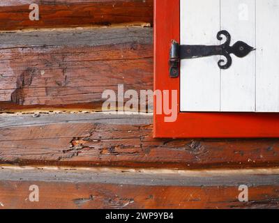 Ethno-Folk Holzläden an einem Fenster mit Holzrahmen, rot-weiß gestrichen. Metallschlaufe in Form eines Pfeils und eines Herzens Stockfoto