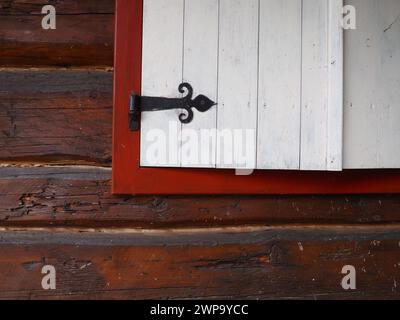 Ethno-Folk Holzläden an einem Fenster mit Holzrahmen, rot-weiß gestrichen. Metallschlaufe in Form eines Pfeils und eines Herzens Stockfoto