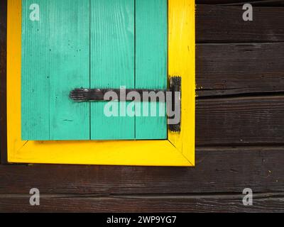 Ethno-Folk Holzläden an einem Fenster mit Holzrahmen, grün und gelb lackiert. Altes serbisches Haus, außen. Architektonischer Komplex Stanisici Stockfoto