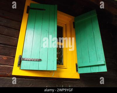 Ethno-Folk Holzläden an einem Fenster mit Holzrahmen, grün und gelb lackiert. Altes serbisches Haus, außen. Architektonischer Komplex Stanisici Stockfoto