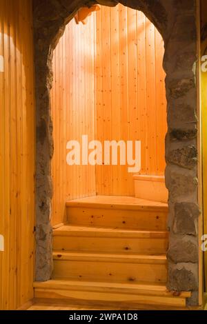 Bogengang aus Feldstein und verwinkelte Kiefernholztreppe, die zum Erdgeschoss in einem alten Haus führt. Stockfoto