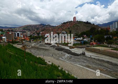 La Paz, BOLIVIEN; 6. März 2024: Instandhaltungsteams, die für die Stadtverwaltung von La Paz arbeiten, beseitigen Hochwasserschutt und Kanäle im Fluss La Paz in der unteren Zona Sur. Februar ist die Regenzeit und dieses Jahr war einer der nassesten Monate der Geschichte. Starke Regenfälle haben Sturzfluten, Erdrutsche und Erosion in vielen Flusstälern und steilen, instabilen Hängen verursacht, die heute Teil der Vororte der Stadt sind. Im Vordergrund dieses Bildes wurden Abschnitte einer unvollendeten Verbindungsstraße zwischen den Bezirken Seguencoma und Mallasa weggespült. Stockfoto