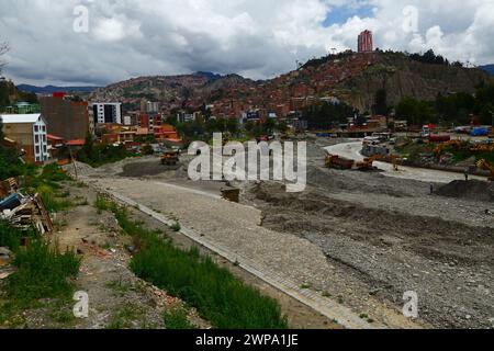 La Paz, BOLIVIEN; 6. März 2024: Instandhaltungsteams, die für die Stadtverwaltung von La Paz arbeiten, beseitigen Hochwasserschutt und Kanäle im Fluss La Paz in der unteren Zona Sur. Februar ist die Regenzeit und dieses Jahr war einer der nassesten Monate der Geschichte. Starke Regenfälle haben Sturzfluten, Erdrutsche und Erosion in vielen Flusstälern und steilen, instabilen Hängen verursacht, die heute Teil der Vororte der Stadt sind. Im Vordergrund dieses Bildes wurden Abschnitte einer unvollendeten Verbindungsstraße zwischen den Bezirken Seguencoma und Mallasa weggespült. Stockfoto