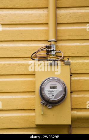 Gelb lackiertes digitales Wasserkraftverbrauchsmessgerät an der Außenwand des Hauses. Stockfoto