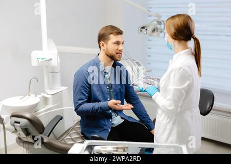 Junger attraktiver Zahnarzt-Besuch, sitzt im Zahnarztstuhl in der modernen Leichtklinik. Junge Zahnärztin mit Röntgenbild Stockfoto