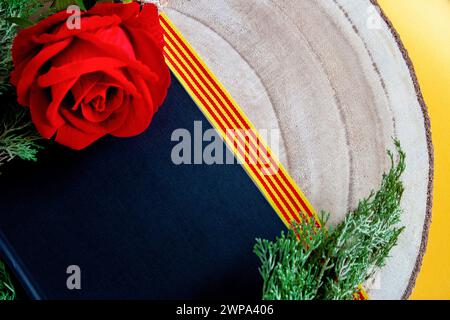 Schwarzes Cover-Buch mit einer roten Rose auf einem Holzstamm und einem Band der katalanischen Flagge Stockfoto