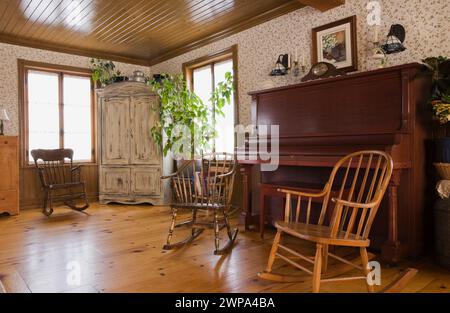 Schaukelstühle, aufstehendes Klavier und antiker Schrank im Wohnzimmer mit Kiefernholzdielen im reproduzierten alten Haus aus den 1800er Jahren. Stockfoto