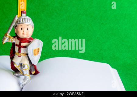 Figur von Sant Jordi auf einem offenen Buch mit leeren Seiten, mit der Flagge von Katalonien und einem grünen Filzhintergrund. Das Konzept des Buchs und des Rosentages. Stockfoto