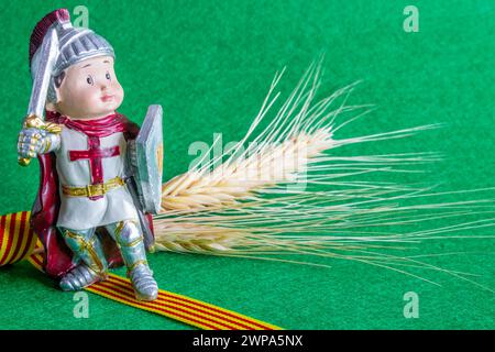 Figur von Sant Jordi mit der katalanischen Flagge auf grünem strukturiertem Hintergrund und Weizenohren Stockfoto