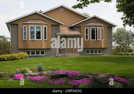 Moderner zweistöckiger brauner Backstein mit hellbraunem Schrankverbund und angelegtem Vorhof mit pinkfarbenen Phlox subulata im Frühjahr. Stockfoto