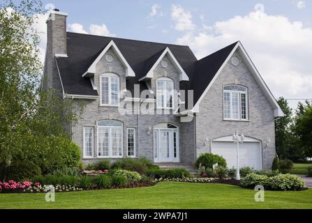 Zeitgenössisches zweistöckiges graues Backsteingebäude mit weißem Zierwerk und landschaftlich gestaltetem Vorhof im Frühjahr. Stockfoto