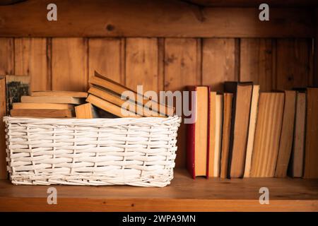 Alte Bücher in einem weißen Korb auf dem Bücherregal Stockfoto