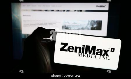 Person, die ein Mobiltelefon mit dem Logo des US-amerikanischen Videospielunternehmens ZeniMax Media Inc. Vor der Webseite des Unternehmens hält. Schwerpunkt auf dem Display des Telefons. Stockfoto