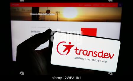 Person mit Smartphone mit Logo des deutschen Verkehrsunternehmens Transdev GmbH vor der Website. Schwerpunkt auf dem Display des Telefons. Stockfoto