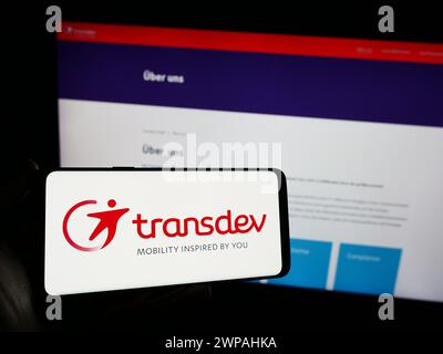Person, die ein Mobiltelefon mit dem Logo des deutschen Verkehrsunternehmens Transdev GmbH vor der Business-Webseite hält. Schwerpunkt auf dem Display des Telefons. Stockfoto