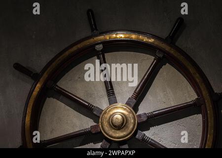 Das Vintage-Lenkrad aus Holz mit glänzenden Messingdetails ist auf einer grauen Betonwand angebracht Stockfoto