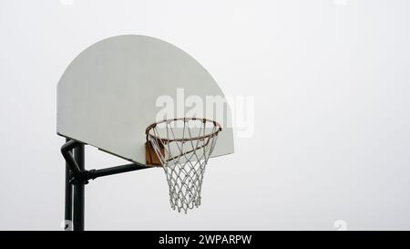 Ein einzelner Basketballkorb mit weißem Rückenbrett und orangefarbenem Rand steht hoch und wartet auf den Beginn eines Spiels. Stockfoto