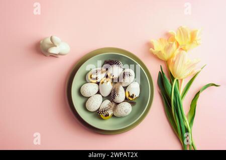 Ostern Hintergrund mit Teller mit Ostereiern, gelben Tulpen und Häschen auf rosa Tisch. Draufsicht, flach, Kopierbereich. Stockfoto