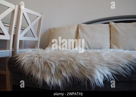 Graues Sofa mit boucle-Polsterstoff und weißen dekorativen geriffelten Kissen. Weißer Teppich oder Bettüberwurf aus Kunstfell mit langem Stapel. Wohnzimmer Stockfoto