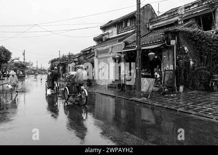 Hoi an, Vietnam; Straßenszene aus der Altstadt. Leute mit dem Fahrrad Taxis bei strömendem Regen Stockfoto