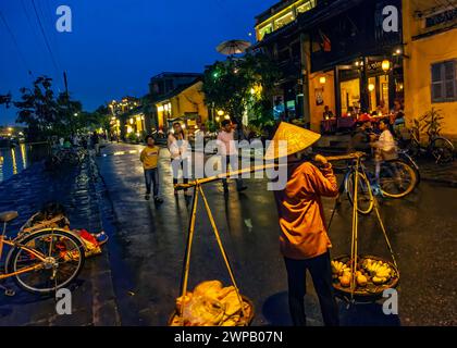 Hoi an, Vietnam; nächtliche Straßenszene aus der Altstadt. Eine junge Frau, die ihre Waren auf einer Bambusstange trägt Stockfoto