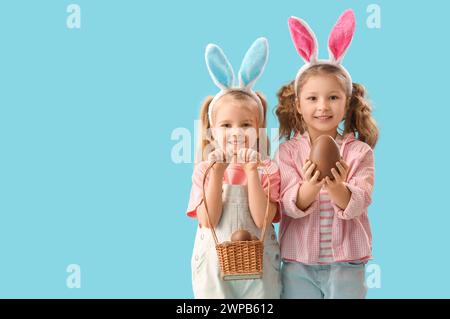 Süße kleine Mädchen in Hasenohren mit Schokoladen-Ostereiern auf blauem Hintergrund Stockfoto