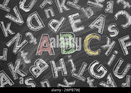 Die Buchstaben des englischen Alphabets werden mit Kreide auf eine Schultafel gezeichnet. Stockfoto