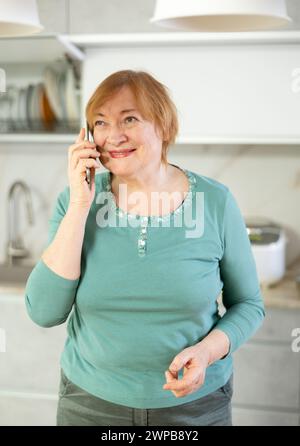 Lächelnde ältere Frau, die mit jemandem auf ihrem Handy spricht Stockfoto