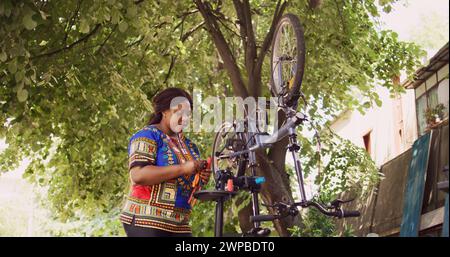 Junge gesunde schwarze Frau, die professionelles Toolkit untersucht und Fahrrad repariert. Sportliche Radfahrerin, die verschiedene Spezialausrüstung für die Wartung beschädigter Motorräder im Hof hält. Stockfoto