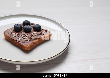 Toast mit leckerer Nussbutter, Heidelbeeren und Nüssen auf weißem Holztisch, Nahaufnahme. Leerzeichen für Text Stockfoto