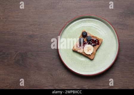 Toast mit leckerer Nussbutter, Marmelade, Heidelbeeren, Nüssen und Banane auf Holztisch, Blick von oben. Leerzeichen für Text Stockfoto