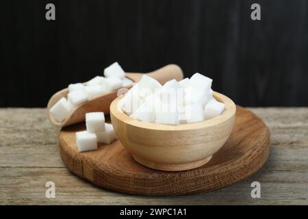 Weiße Zuckerwürfel in Schüssel und Schaufel auf Holztisch vor dunklem Hintergrund, Nahaufnahme Stockfoto