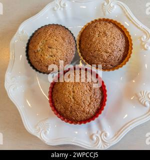 Drei hausgemachte, frisch gebackene Bananennußmuffins in Silikonbechern auf einer weißen Platte von oben. USA. Stockfoto