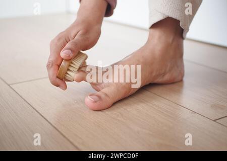 Mit einer Bürste bürstet die Person sanft ihren Fuß auf den Hartholzboden Stockfoto