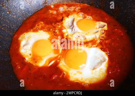 Shakshuka, pochierte Eier in würziger Tomatensauce, die in einer gusseisernen Pfanne gekocht werden Stockfoto