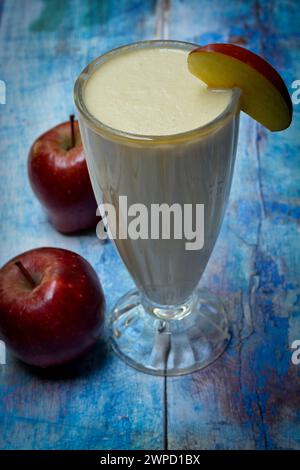 Ein Apfelmilchshake in einem Glas und Äpfel auf einem Holztisch verstreut. Stockfoto