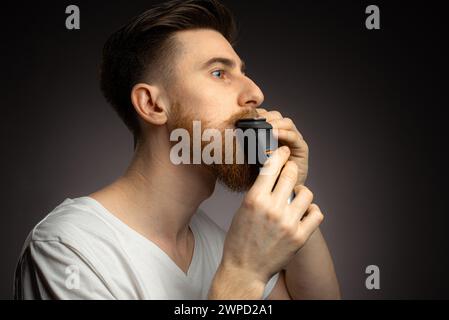 Hübscher junger bärtiger Mann trimmen seinen Bart mit einem Langhaarschneider Stockfoto