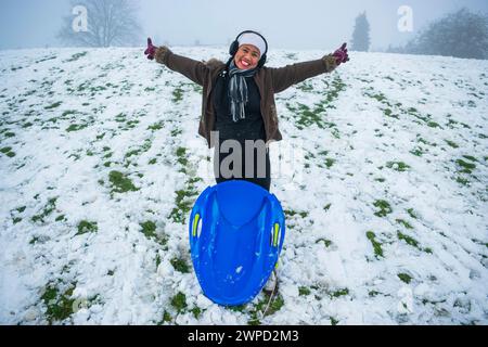 Eine philippinische Frau, die zum ersten Mal Spaß beim Schlitten im britischen Snow, Sledding, South Yorkshire, England hat Stockfoto
