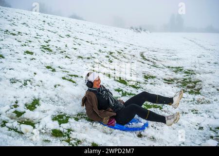 Eine philippinische Frau, die zum ersten Mal Spaß beim Schlitten im britischen Snow, Sledding, South Yorkshire, England hat Stockfoto